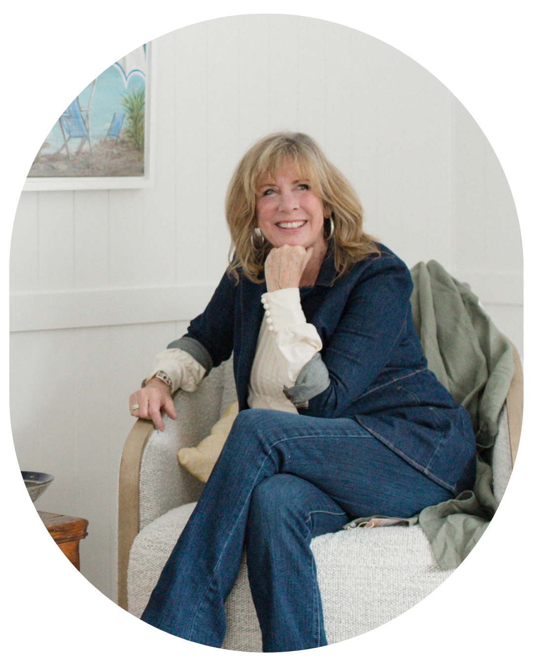 Anne of the Robin Nest, woman wearing denim with white blouse smiling with her head resting on her hand