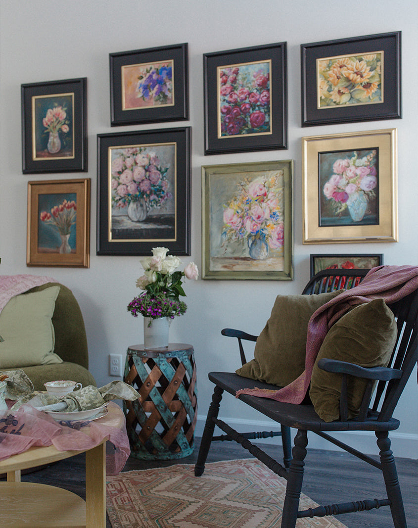 Floral framed artwork hanging on white wall above dark black bench and green and pink sofa
