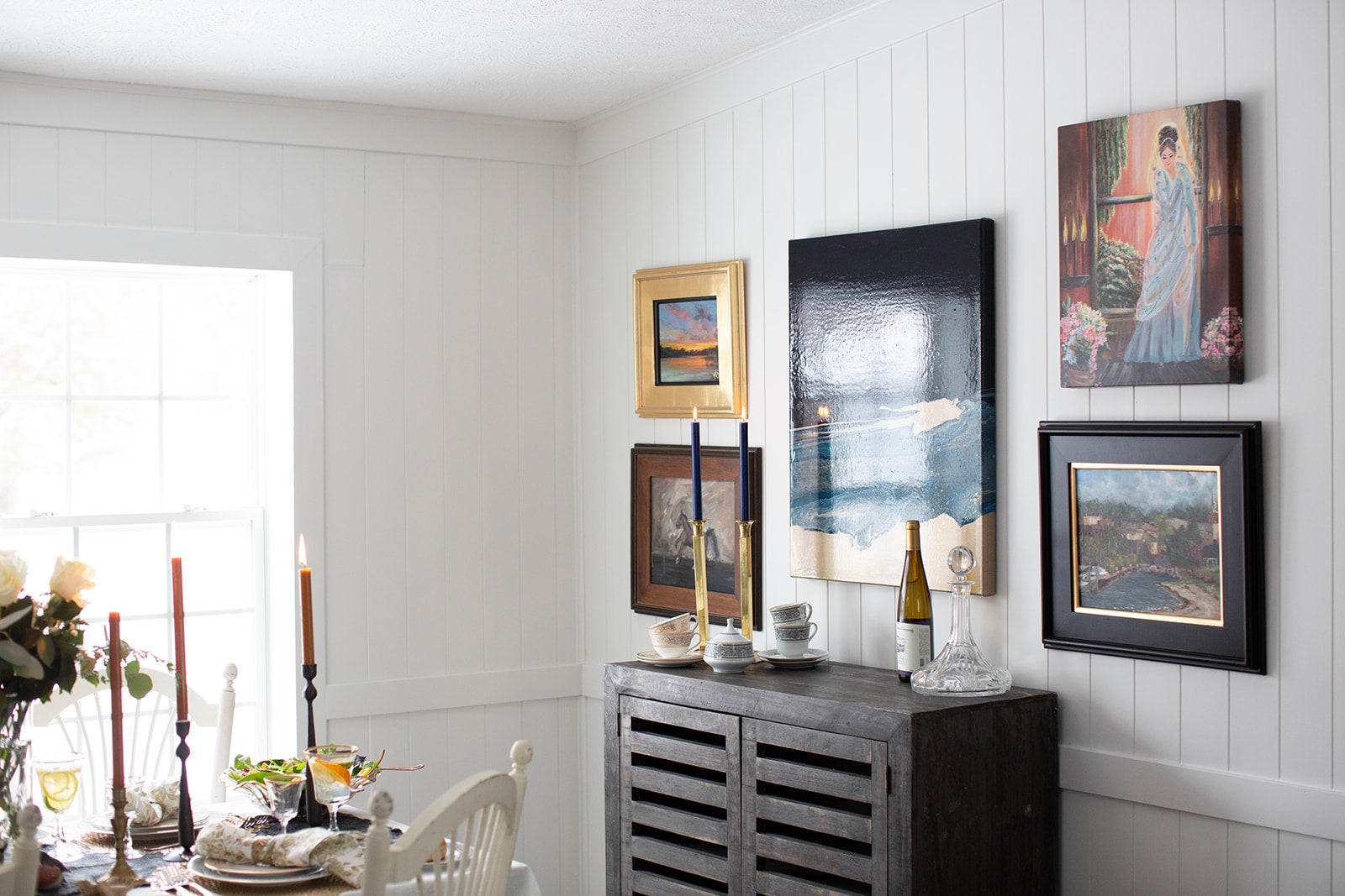 Artwork hanging on white panel wall above dark cabinet in dining room