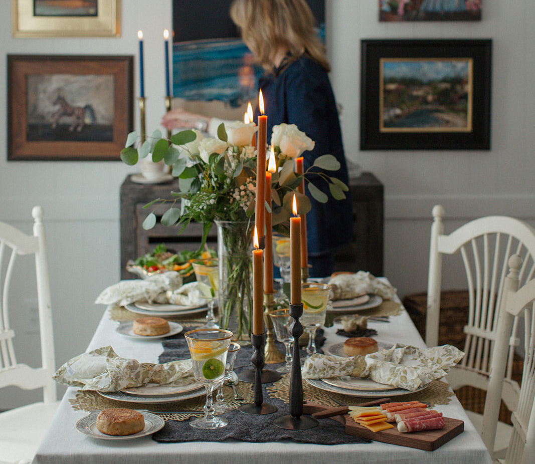 Candles on dining room table with variety of linen, wood, metal, and glass textured decor